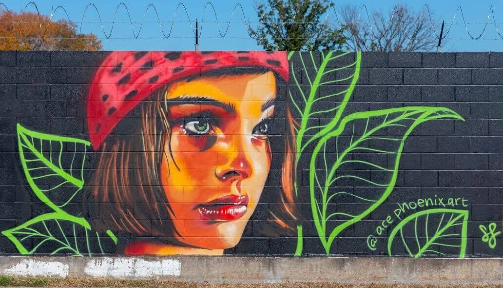 Mural of a woman's face surrounded by leaves with a green outline against a black background along the outer wall of the Kashmere bus operating facility at 5700 Eastex Freeway in Houston